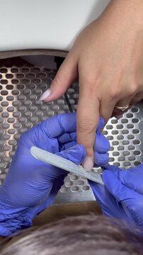 Video of a nail technician filing nails. Manicurist shapes nail using salon nail file during cosmetic procedure in beauty salon. Woman gets a french manicure at a beauty salon, manicurist files her cu