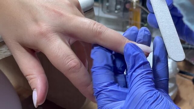 Video of a nail technician filing nails. Manicurist shapes nail using salon nail file during cosmetic procedure in beauty salon. Woman gets a french manicure at a beauty salon, manicurist files her cu