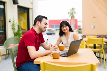 Young adults working together at outdoor cafe, using laptop for remote work and digital...