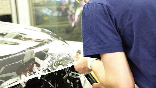 A car wrapping specialist applies a PPF or vinyl film to the body car. Selective focus. PPF protective film. The process of installing vinyl PPF film on the car. Protects the paint from scratches. 