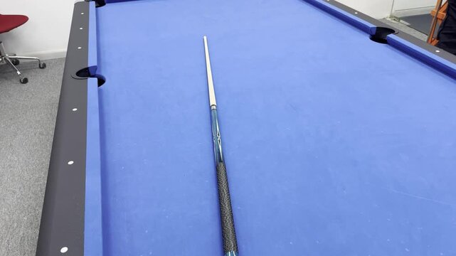Billiard cue stick lying on an empty blue pool table