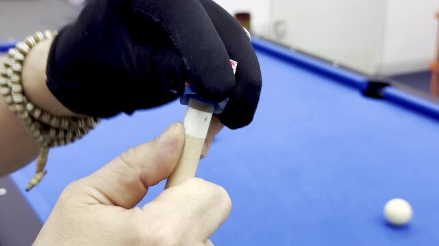 Extreme close up of pool player with black glove applying blue chalk to billiard cue
