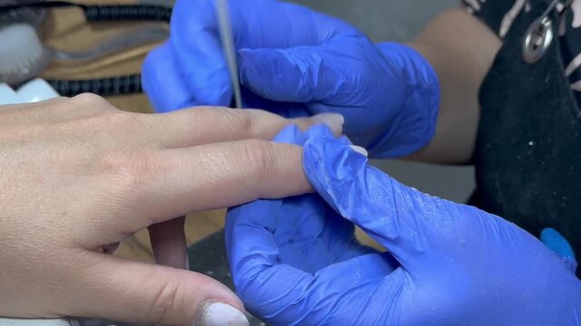 Video of a nail technician filing nails. Manicurist shapes nail using salon nail file during cosmetic procedure in beauty salon. Woman gets a french manicure at a beauty salon, manicurist files her cu