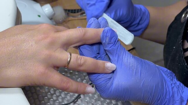 Video of a nail technician filing nails. Manicurist shapes nail using salon nail file during cosmetic procedure in beauty salon. Woman gets a french manicure at a beauty salon, manicurist files her cu