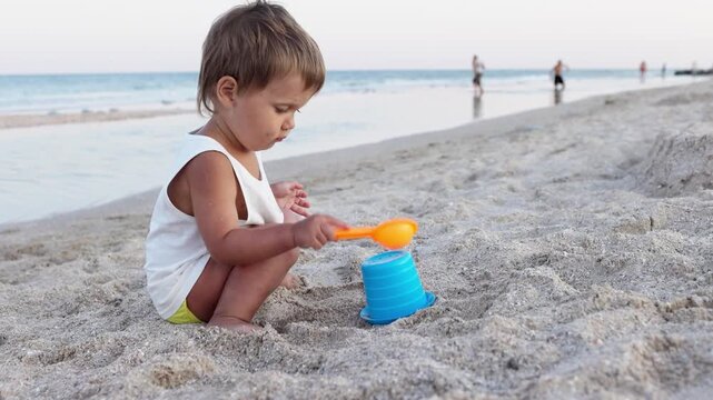 Boy playing with toys on the beach building beads and turrets smiling at someone behind the scenes on summer vacation