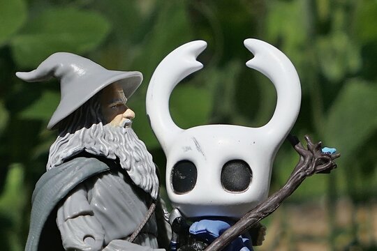 Action figure of wizard Gandalf from Lord Of The Rings and Hobit novels of J.R.R. Tolkien with figure of insectoid main hero of platformer game Hollow Knight, sunlit by spring daylight sunshine. 