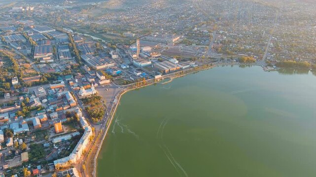 Russia, Votkinsk. Votkinsk Reservoir embankment, industrial waterfront with factories and dam infrastructure, aerial panoramic view at sunset with golden light over the water. Drone footage
