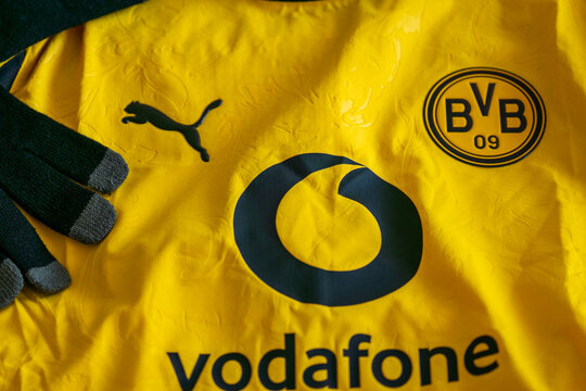 Bratislava, Slovakia, Europe - May 01, 2026: official yellow and black borussia dortmund football jersey shirt with vodafone logo lying next to a black baseball team cap looking away
