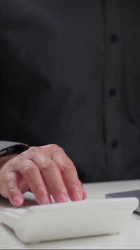 Male clerk taps small keys inside room, counting cost data near desk pc, managing firm cash, checking tax files, planning work goals, keeping clear audit logs every day.