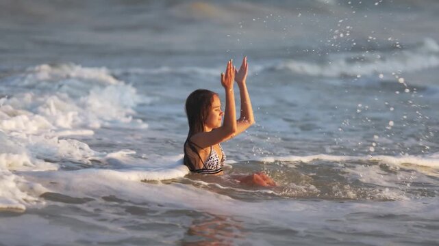 Girl with wet hair in a leopard swimsuit splashes water while sitting in the sea