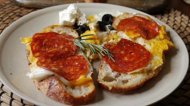 Open face breakfast toast with fried egg chorizo sausage feta cheese black olive rosemary on plate with sourdough bread