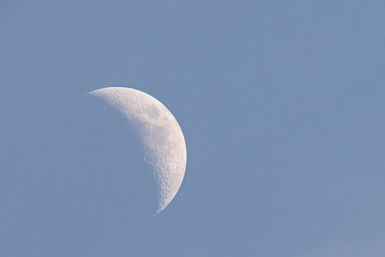 Visual representation of crescent moon with prominent craters and twilight background