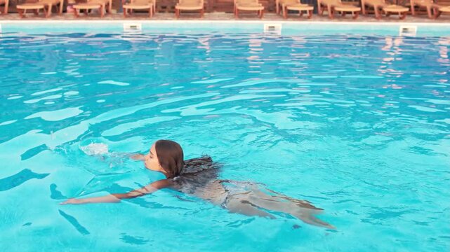 Girl in leopard swimsuit playing in the pool under the summer sun