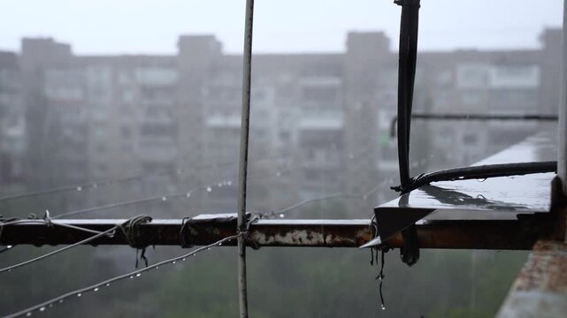 Heavy Rain Dripping from Old Rusty Balcony Window Cornice and Clothesline Ropes with Water Drops, Cinematic Out of Focus Multi Story Residential Building in Soviet Block Style on Background, 4K