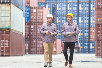 Fototapeta premium Two logistics managers walking and discussing work at a busy shipping container terminal, Industrial cargo operations team coordinating shipment logistics at a global shipping yard