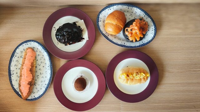 Top view of assorted pastries and savory buns on plates with chocolate glaze, cream topping and bread on a wooden table.