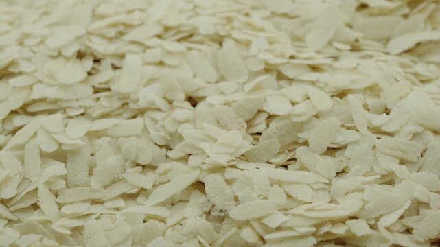 closeup of raw white flattened rice flakes, known as poha. A staple Indian breakfast ingredient, these dry organic cereal flakes background texture rotation turntable video footage