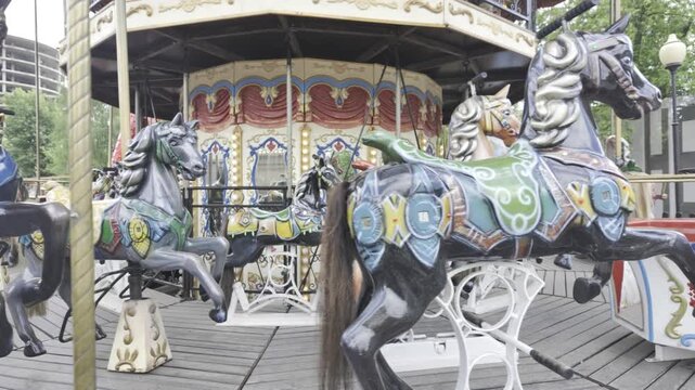 A vintage carousel horse with ornate colorful patterns rotates outdoors. The wooden black stallion features intricate traditional decorations.