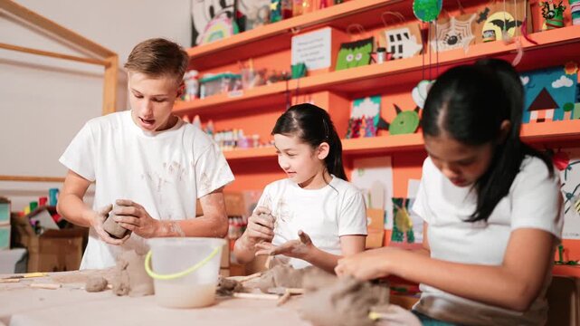 Happy diverse high school student modeling clay at pottery workshop. Cute children with mixed raced working and making cup of clay by using carving equipment at art lesson. Creative class. Edification