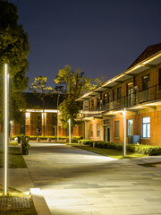 Fototapeta premium Empty paved pedestrian street lined with illuminated brick buildings and modern streetlights at night