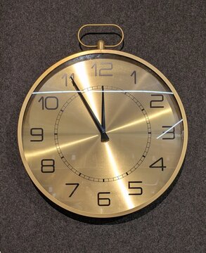 Vista de cerca de un reloj decorativo de pared con el dise&ntilde;o de un reloj de bolsillo vintage en acabado dorado met&aacute;lico, en pared de color gris	