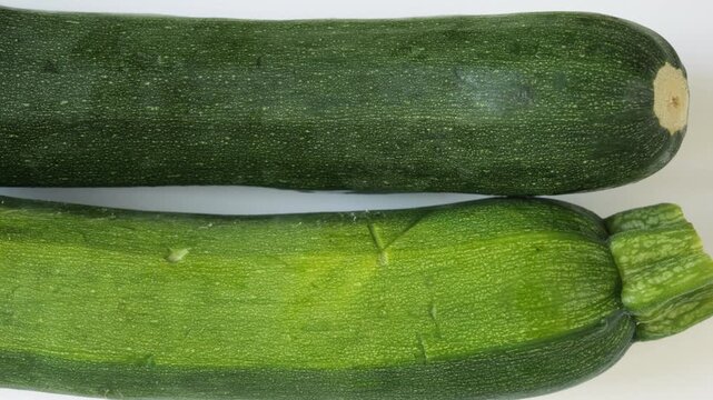 Fresh green zucchini slowly moving isolated on white background