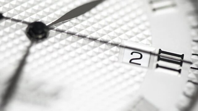 Macro video of white classic luxury watch face with black hands moving across textured dial surface.