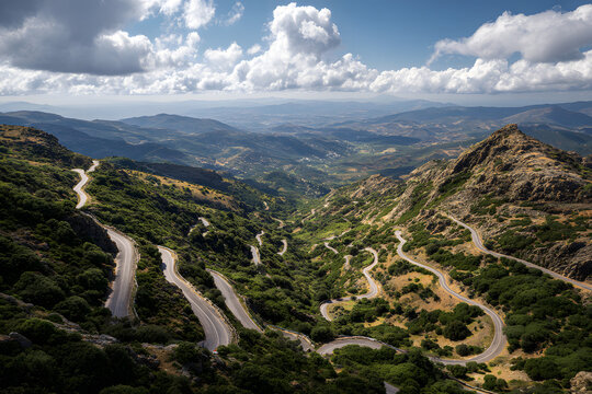 Aerial view of a winding mountain road through a lush green forest with countless switchbacks, descending towards a misty coastal landscape.