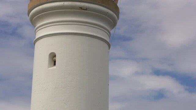Camera panning up historic Kiama Lighthouse NSW with blue sky and fluffy clouds coastal landmark