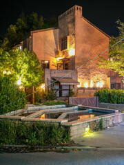 Fototapeta premium Illuminated traditional building with stone water feature in garden at night