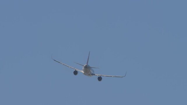 A commercial passenger jet airplane climbing high into a clear solid blue sky. Rear perspective view showing the tail, engine exhausts, and winglets on the wingtips during a smooth flight departure.