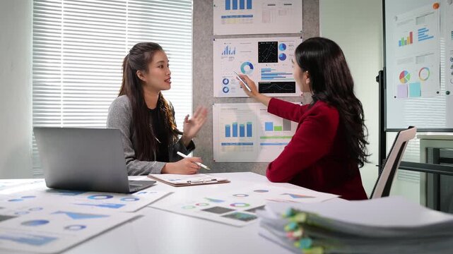 Young Asian businesswoman discussing financial data and analyzing company growth on a chart during a collaborative office meeting.