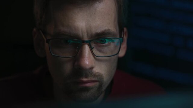 Close-up portrait of a focused software engineer working on a complex artificial intelligence or data science script at night, green programming code lines reflecting in his eyeglasses. 