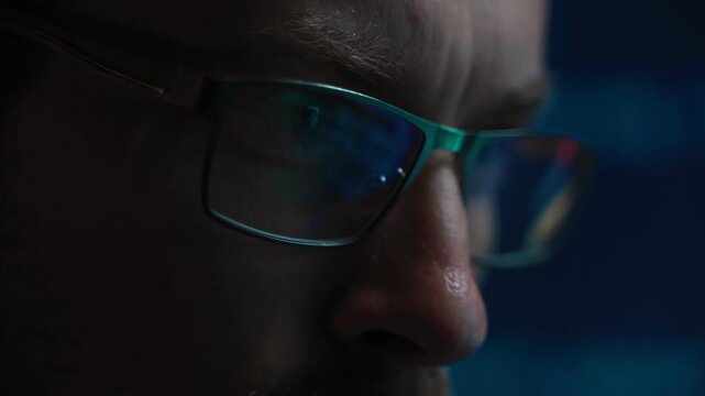 Close-up of developer eyes in a dark room, code reflecting vividly in his glasses. Data scientist stares intently at digital scripts, working on a machine learning or artificial intelligence project.