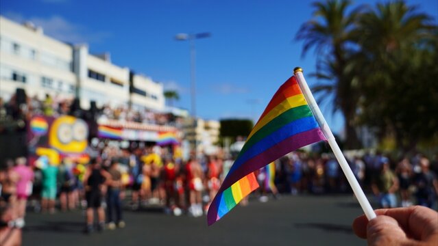 Hand holding a rainbow flag, symbolizing LGBTQ+ freedom and diversity, while celebrating amidst a vibrant crowd during the Maspalomas gay pride festival parade on a sunny day