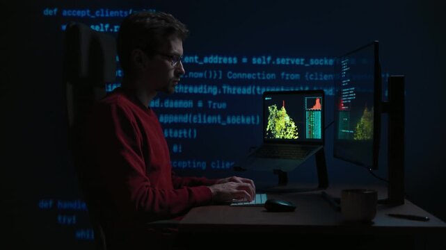 Side view, coder at a dark office desk works across multiple screens at night, with programming script on a background. Data scientist working on a machine learning or artificial intelligence task.