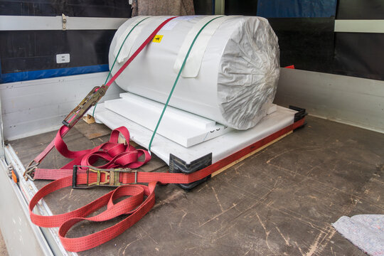 Large white industrial material roll secured with red and green cargo straps on a pallet inside a delivery truck. Useful for freight transport, logistics, packaging, warehouse delivery, cargo safety, 