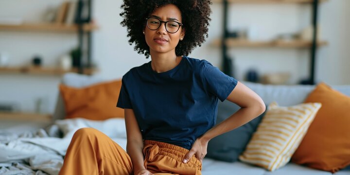 Woman holding lower back seated on living room couch