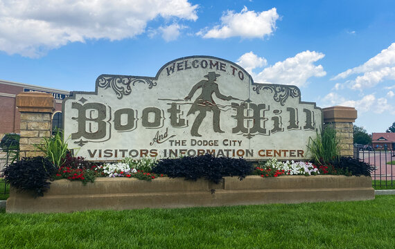 Large stone welcome sign for Boot Hill at the Dodge City Visitors Center, featuring a cowboy silhouette, floral landscaping and blue sky, evoking historic western tourism and local heritage.