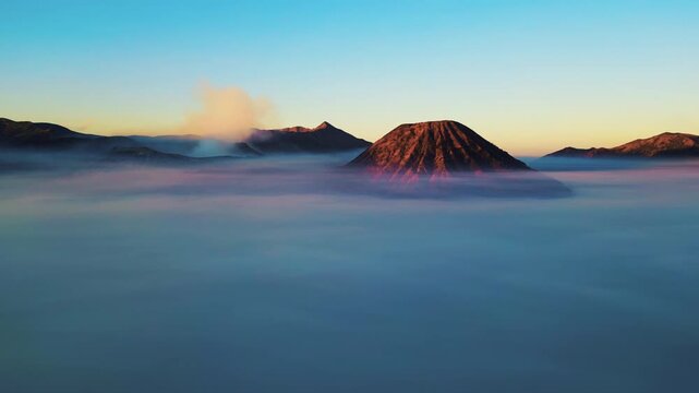Cinematic aerial view of Mount Bromo volcano at sunrise &ndash; Breathtaking drone shot of smoking crater and mystical sea of sand covered in morning mist, East Java Indonesia landscape 4k