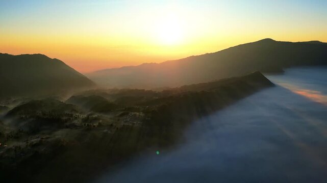 Spectacular drone flyover of active Mount Bromo caldera &ndash; Amazing volcanic dust and sulfur smoke rising in warm golden hour light, premium Indonesia tourism and travel advertising background
