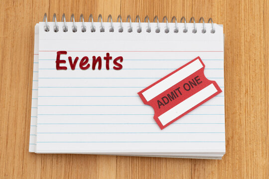 Events text on a spiral notebook of index cards with admit one ticket on wood desk