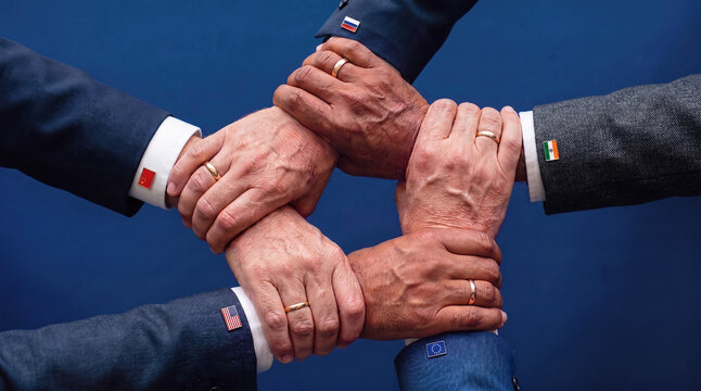 Five interlocking hands with international flag pins on suit cuffs symbolizing global cooperation and alliance