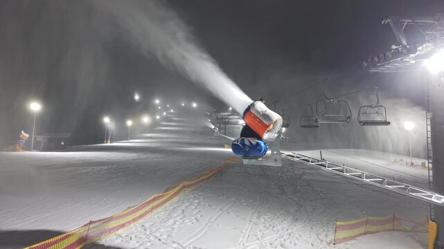 Artificial Snow Display. Operator Sprays Thick Artificial Snow Onto Illuminated Ski Run With Fencing