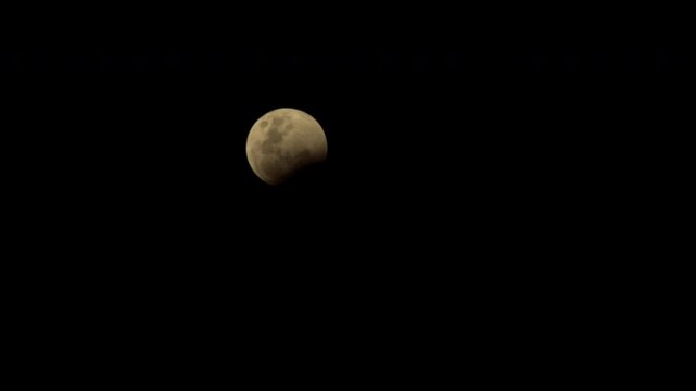 Timelapse of orange moon moving across night sky as dark clouds pass in front of lunar surface
