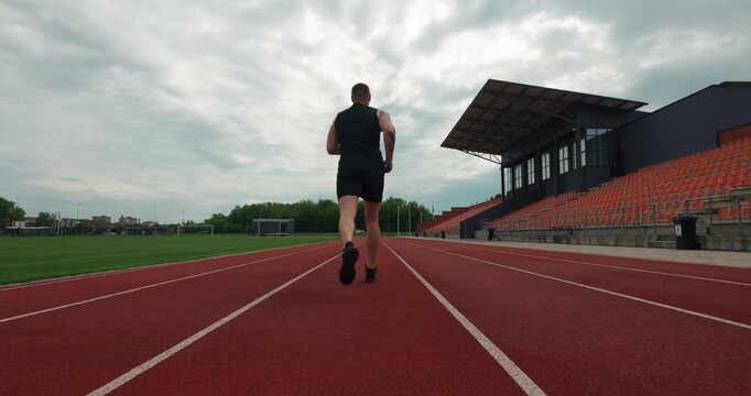 Steadicam follow shot of an athletic man running on a stadium track in slow motion