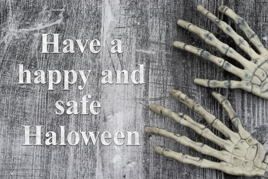 Have a happy and safe Halloween text with skeleton hands reaching on weathered wood