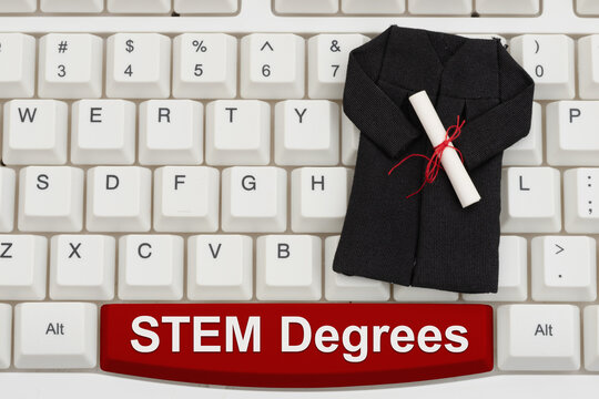 STEM degree text with a grad gown and diploma on white computer keyboard for distance and e-learning