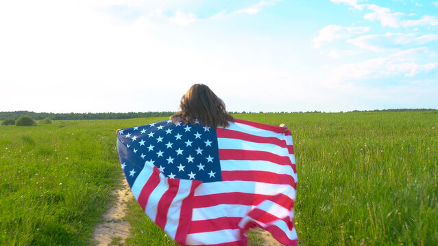 Young caucasian girl with American USA flag running on the rural road in green lawn. Independence day 4th July concept