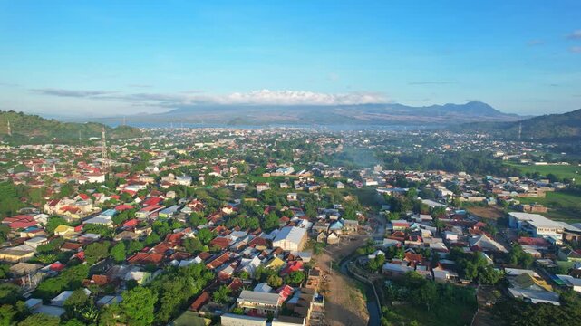Aerial drone footage of Bima city background area, with many buildings and houses, at sunrise with clouds, in Sumbawa island, Indonesia, with Doro Oromboha mountain in background
